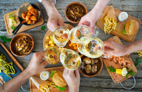 People with white wine toasting over served table with food.