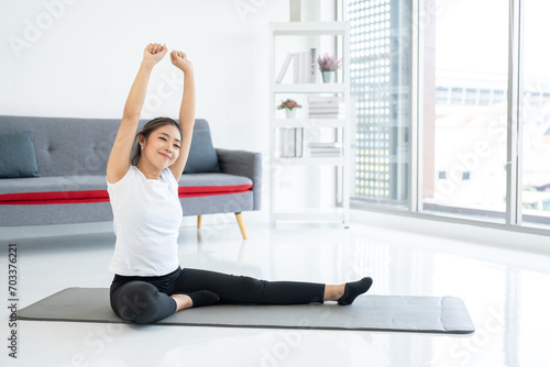 Beautiful smiling Female wearing sportswear exercise training yoga in living room. Attractive asian young fitness woman stretching warming up before workout at home.
