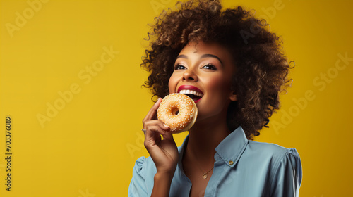 portrait of a african american woman holding eating donut isolated on yellow background, junk unhealthy food diet concept copy space, Valentine day, sweet tasty life