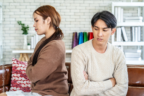 Photo of resentful asian guy and girl acting like arguing couple and not speaking to each other, while sitting together on couch at home photo