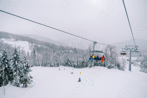 Tourists ride on a chairlift above the forest and ski slope with skiers skiing