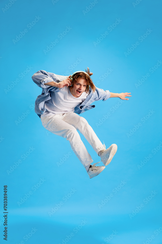 Full-length portrait of young man, dressed fashion casual outfit and jumps with joy and joy listening to music in modern headphones. Concept of self-expression, human emotions, retro music and party.