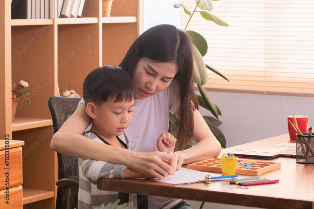 Happy Asian single mother multitask spent time playing alphabet toys and drawing with little boy while working freelance or creative design remote work from home, young teacher teaching preschool kid Happy Asian single mother multitask spent time playing alphabet toys and drawing with little boy while working freelance or creative design remote work from home, young teacher teaching preschool kid