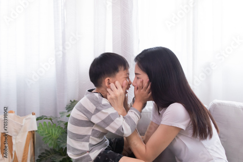 Happy family Asian mother and son playing together touching cheeks each other laughing out loud kidding with fun indoor at home weekend holiday, mom and kid bonding relationship, motherhood tenderness