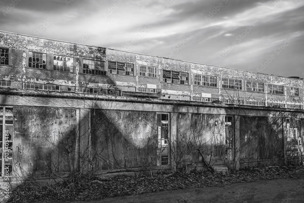 Exterior facade of abandoned 2 storey factory, broken windows, grey scudding sky, nobody