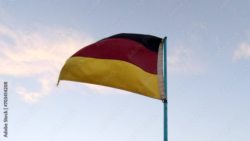 Germany flag on flagpole flutters in the wind, slow motion. A dirty and tattered flag of the Federal Republic of Germany on blue sky with clouds background