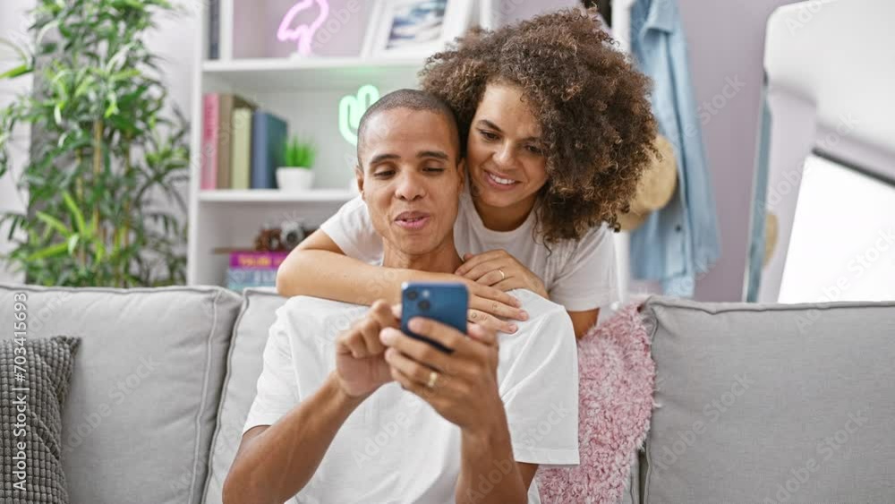 Beautiful couple confidently enjoying a fun-texting session, happily sitting on their home sofa, love radiating from their smiling expressions