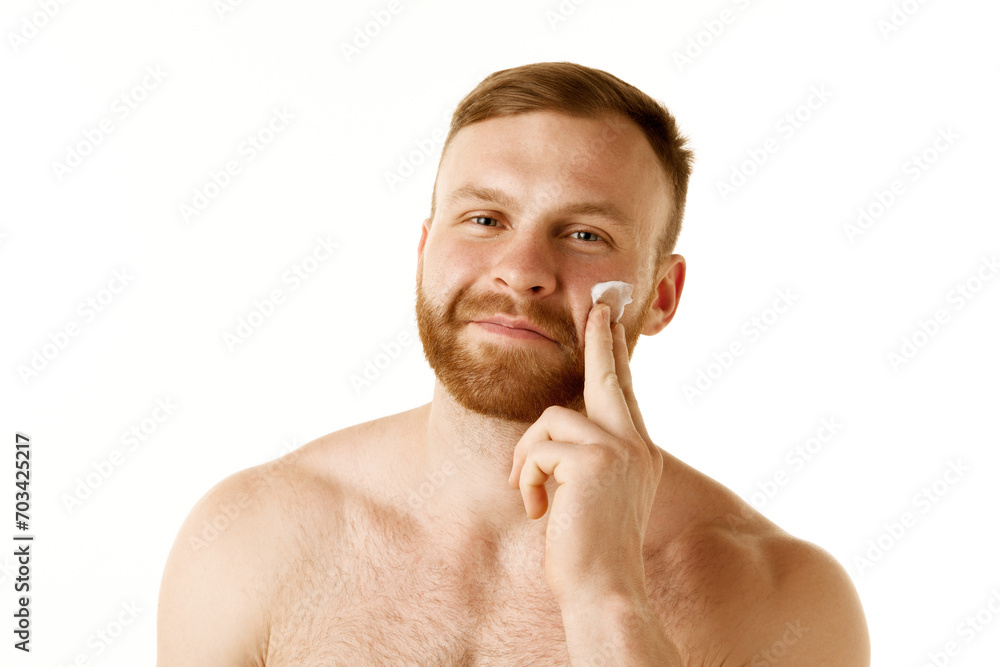 Portrait of naked man with red hair and beard applying anti-aging, skin care product against white studio background. Concept of natural beauty, youth, spa treatment, selfcare, cosmetic. Ad Portrait of naked man with red hair and beard applying anti-aging, skin care product against white studio background. Concept of natural beauty, youth, spa treatment, selfcare, cosmetic. Ad