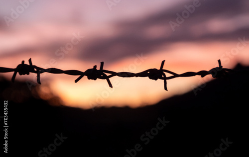 Silhouette of barbed wire on yellow sunset background. barbed wire fence silhouette at orange sunset.