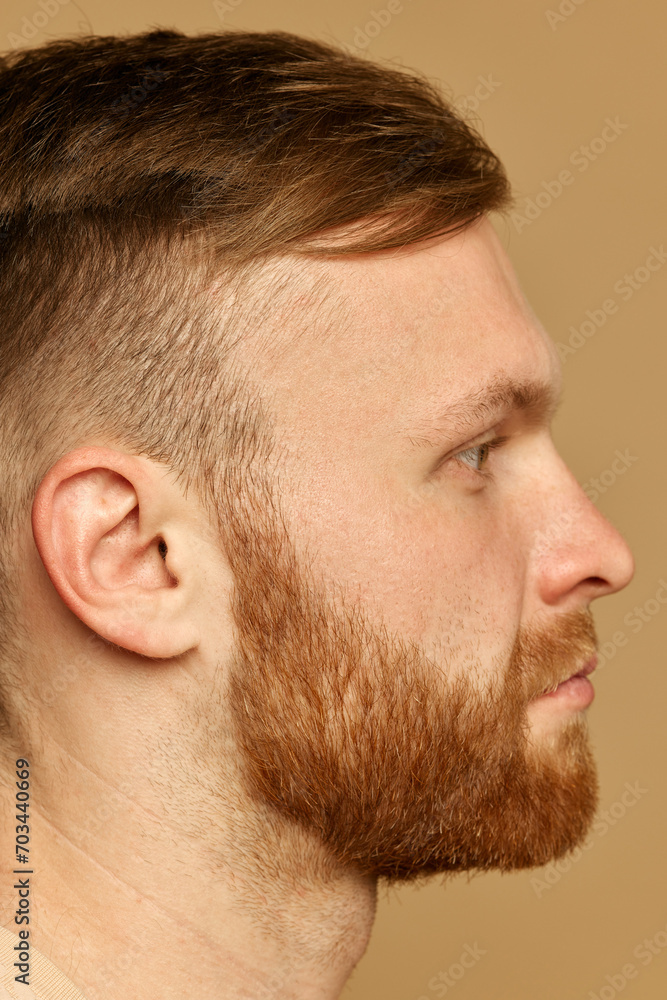 Obraz premium Half face close up portrait of young attractive man with red hair and beard against beige studio background. Male facial care routine. Concept of beauty treatment, selfcare and hygiene, cosmetic, spa.