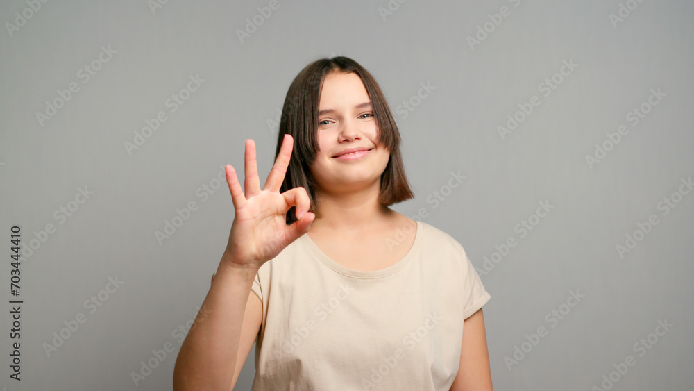 Portrait of attractive cheerful latin teen girl using laptop showing ok-sign winking isolated over gray color background Portrait of attractive cheerful latin teen girl using laptop showing ok-sign winking isolated over gray color background