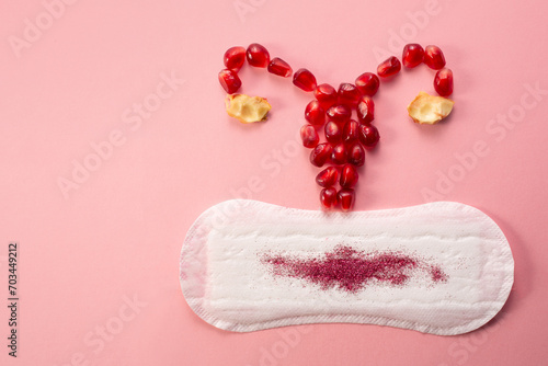 Feminine hygiene pad with and uterus made of pomegranatered. First menstrual period concept on pink background