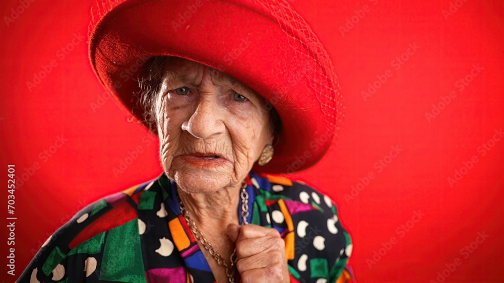 Unhappy displeased fisheye portrait caricature of funny elderly woman saying NO with red hat isolated on red background. Unhappy displeased fisheye portrait caricature of funny elderly woman saying NO with red hat isolated on red background.