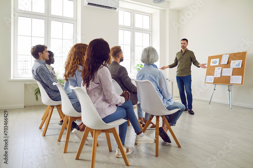 Business coach making a presentation for a diverse audience in an office workplace. Young man sharing his professional experience with a team of corporate workers during a business training meeting photo