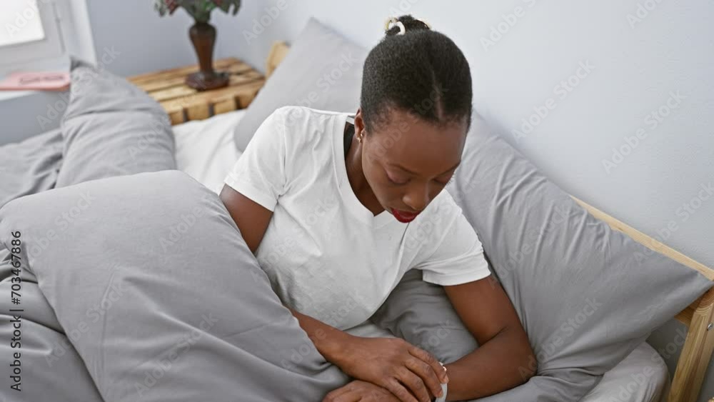 Worried african american woman lying in bed, checking the time on her wristwatch, fearing she's late for work in her bedroom Worried african american woman lying in bed, checking the time on her wristwatch, fearing she's late for work in her bedroom