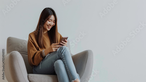 Woman is sitting comfortably in a chair, smiling and looking at her smartphone
