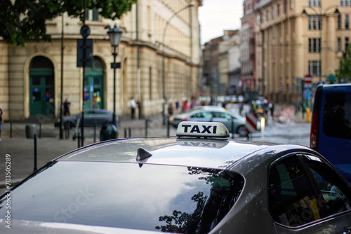 Sign taxi on the car roof that is parked next to cross road in European city. Selective focus, blurred background.