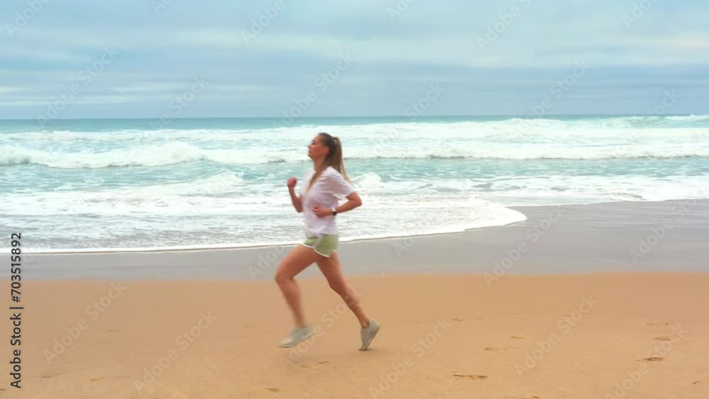An exhilarating aerial drone shot of young woman running along the sandy beach with the sea waves. Embracing a healthy lifestyle and joy of sports by ocean. An exhilarating aerial drone shot of young woman running along the sandy beach with the sea waves. Embracing a healthy lifestyle and joy of sports by ocean.