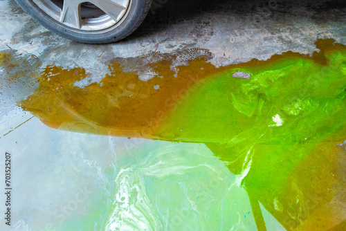 puddle of green coolant and brown technical liquids on the concrete floor near car. photo