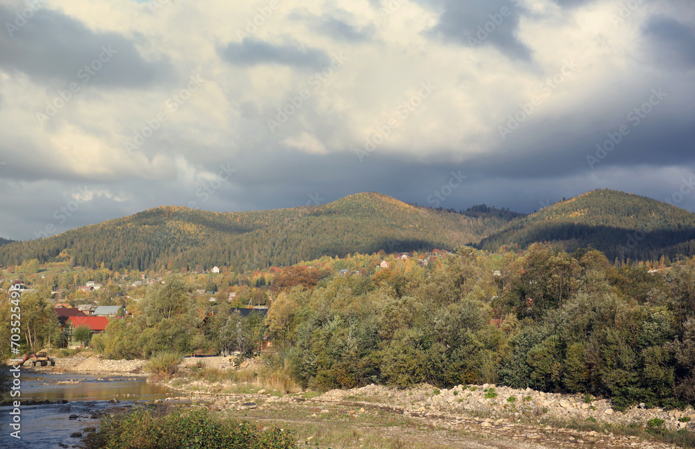 Countryside in mountains at sunrise. Grassy rural slopes with fields and trees in fall foliage in autumn. Magnificent mountain in the hazy distance.