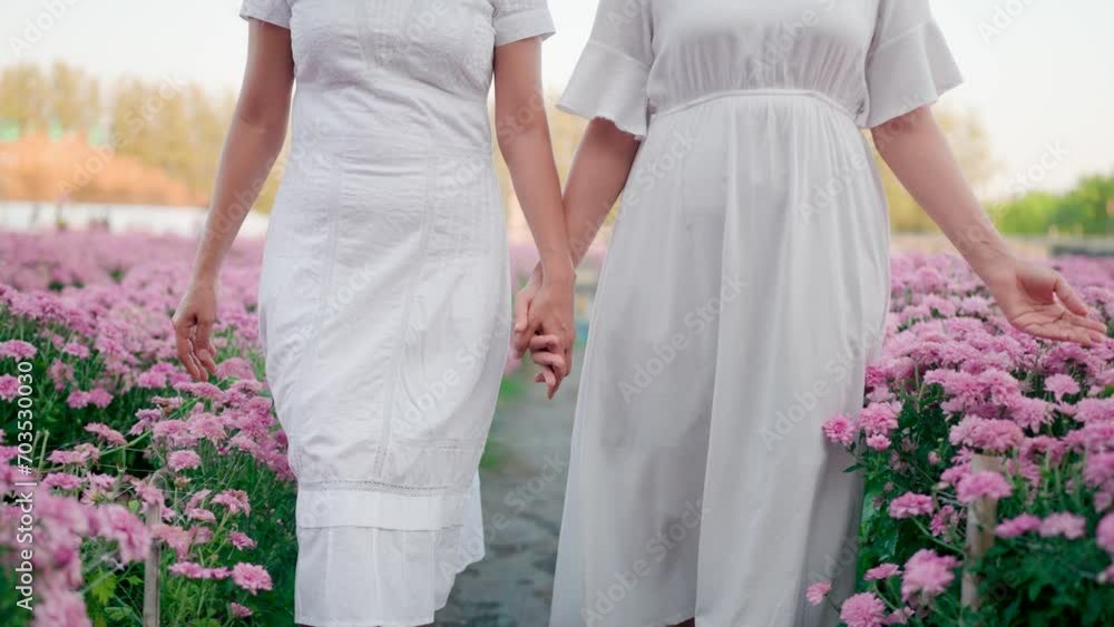 Girl and friend holding hands walking in pink flower garden Girl and friend holding hands walking in pink flower garden