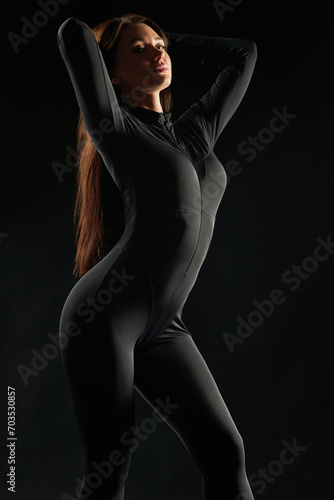 Graceful, relaxed woman wearing black, dancing in low light Illumination. Side view of beauty posing, gently touching long hair, demonstrating body shapes, against black background. Beauty concept.