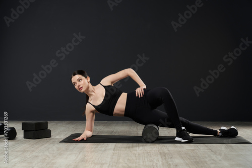 Attractive sportswoman wearing gym clothes, lying on side on yoga mat with foam roller under leg. Advanced female sport instructor using sport equipment while training. Concept of sport, training.