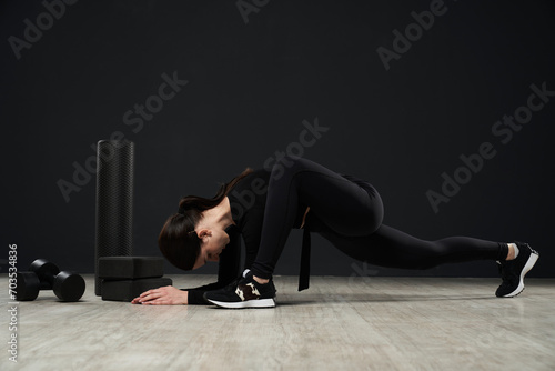 Unrecognizable flexible woman lunging and folding forward in modern gym during workout. Side view of sporty female exercising and stretching with gym equipment in studio. Sport, lifestyle concept. 