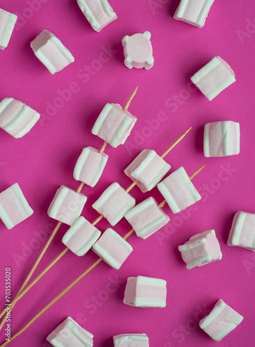 White and pink marshmallows on skewers on a bright pink background