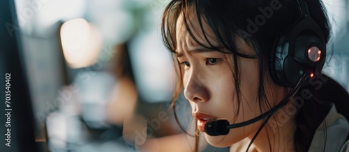 An overwhelmed Asian female call centre operator deals with customer complaints while feeling stressed and exhausted. photo