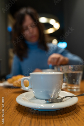 closeup of a cup of cappuccino and a beautiful blurry middle aged woman having breakfast in the background - travel and vacation concept