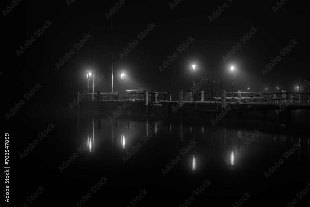Mooring in the harbour for public passenger ship, dark and foggy monochrom picture, the lights reflect in water