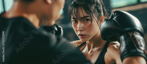 Young Asian woman practicing self-defense at the gym with a male trainer, using boxing gloves and working on uppercut punches during kickboxing training. photo