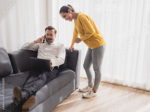 Portrait caucasian senior business man sit sofa and latin woman standing smile happy laptop talking mobile phone plan job work newproject along with look success future agreement in living room office photo