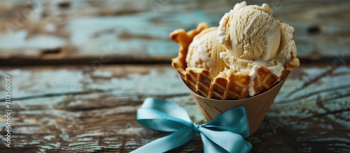 Delicious ice cream in a waffle cup and gift with a blue bow on wooden surface. Space for text.