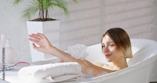 Relaxed caucasian woman washing hands in comfortable warm bath in slow motion. Side view of sexy girl taking bathtub with bubbles and foam in luxury hotel. Concept of spa, recreation, self care.