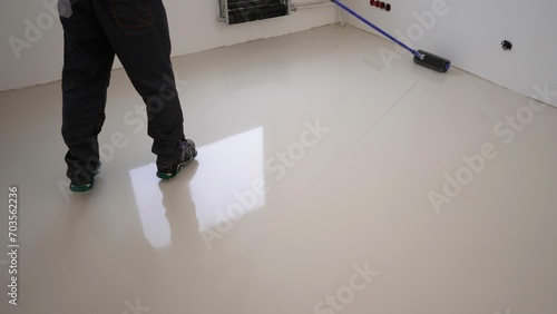 A worker applies gray epoxy resin to a new floor. A worker with a needle roller applies a new concrete screed with self-leveling cement mortar for floors. 