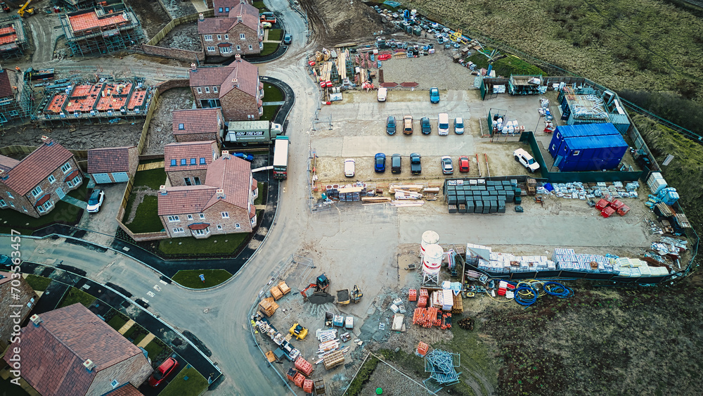 Aerial view of a construction site with materials and equipment near residential houses.