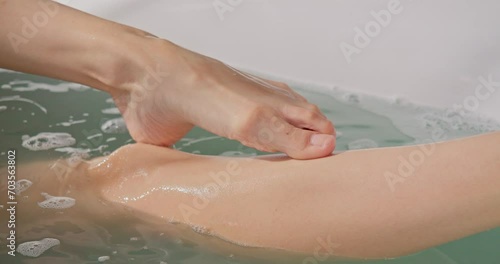 Smooth legs of anonymous woman having relaxing bath, resting after work day. Crop view of female with silky skin, soaking in warm salt bath at home, in slow motion. Concept of relax, spa, body care.