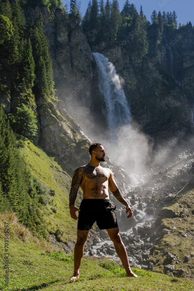 Naklejka premium Man in Alps waterfall. Sexy man. Man freedom lifestyle. Meditating in nature. Hispanic man practicing yoga. Lifestyle relaxation concept, summer meditation on nature. Calmness and relax in nature.