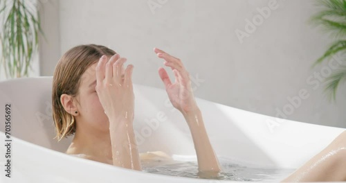 Relaxed beautiful woman taking salt bath at home. Side view of pretty blonde female with closed eyes soaking in modern bathtub at luxury resort, in slow motion. Concept of self care, recreation, spa. 