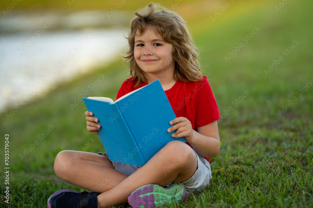 Outdoor portrait of a cute little kid reading a book in summer park. Blond kid boy sitting on grass and reading book. Summer weekend in park. Schoolboy child study with book, learning. Book store. Outdoor portrait of a cute little kid reading a book in summer park. Blond kid boy sitting on grass and reading book. Summer weekend in park. Schoolboy child study with book, learning. Book store.