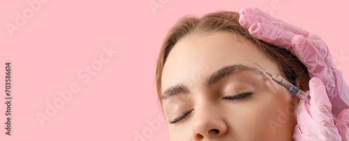 Young woman receiving filler injection in face against pink background with space for text, closeup