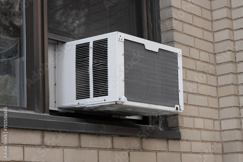 exterior view of air conditioning window unit extruding from the window sill of a beige brick building photo