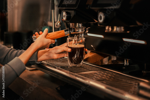 A barista pours fresh coffee into a glass from an espresso machine