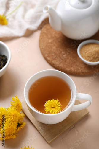 Cup of healthy dandelion tea and teapot on beige background
