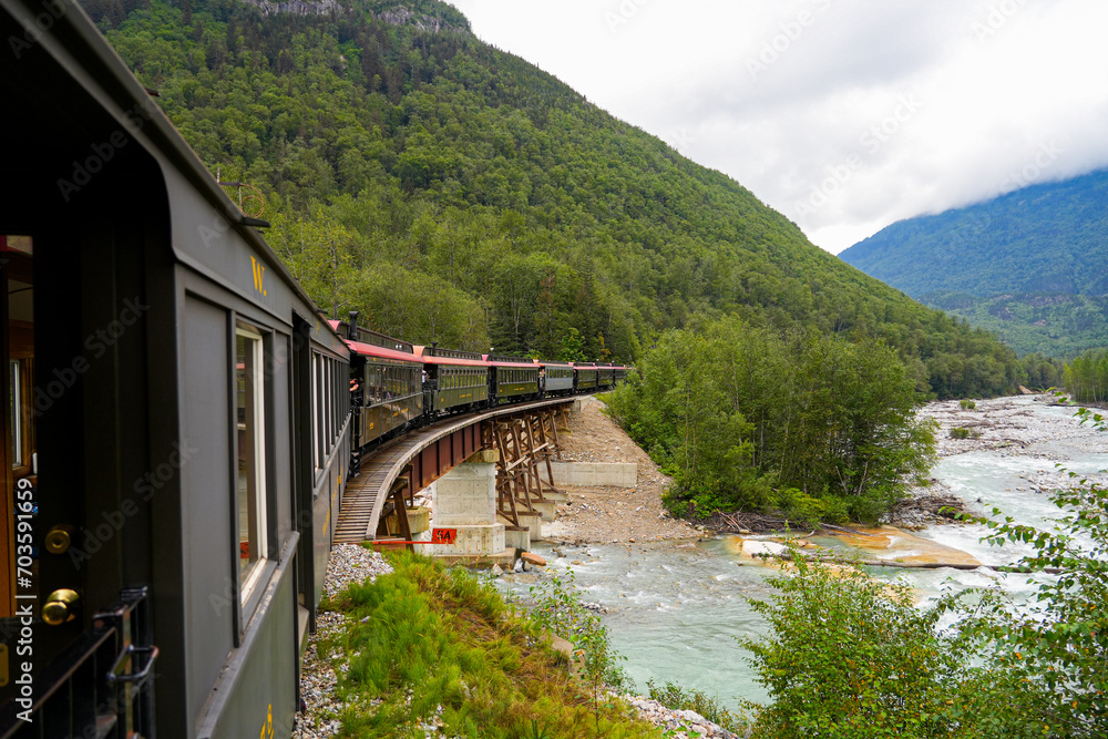 Fototapeta premium Narrow-gauge train of the White Pass and Yukon Route on an old trestles bridge in the Alaskan mountains between Skagway and Canada