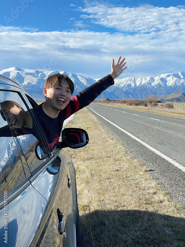 Immerse in the thrill of a solo adventure. A Chinese traveler embraces the scenic road near Christchurch, South Island, with snow-capped mountains framing the journey. Explore the beauty of freedom.