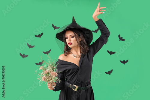 Young witch with herbs and bats on green background