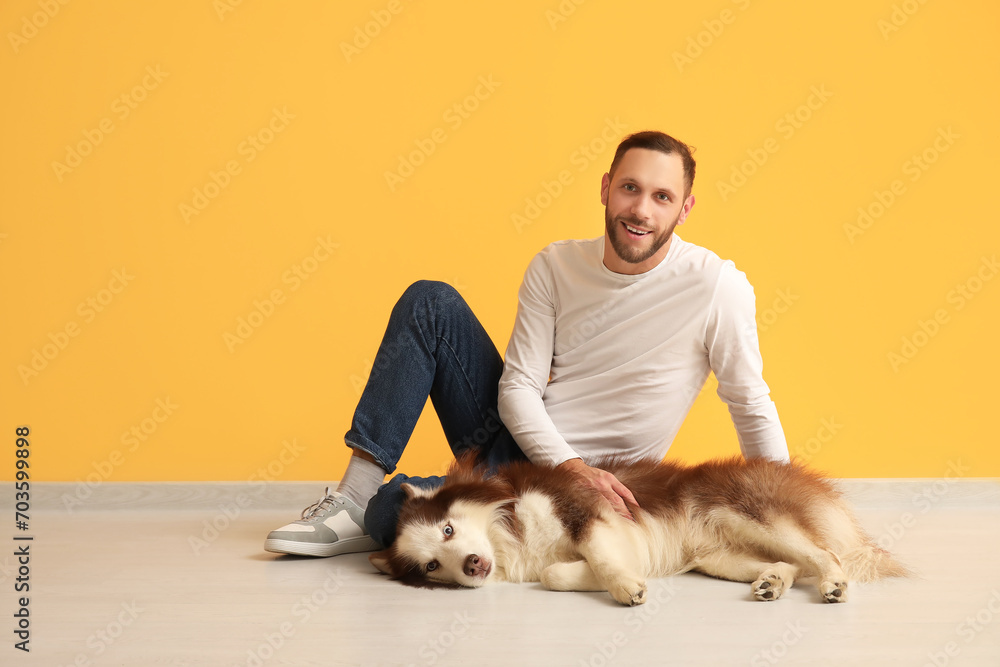 Handsome young man with cute Husky dog near orange wall